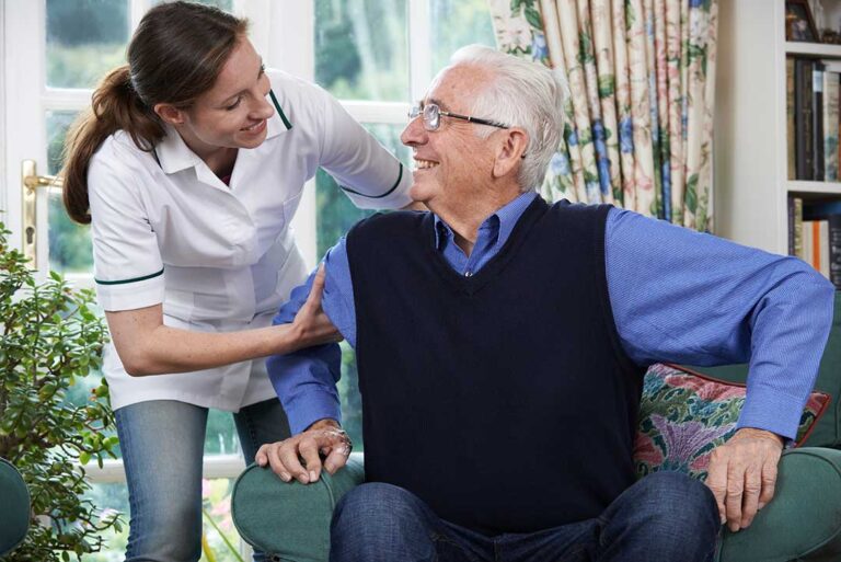 Family members review care documents with an assisted living staff member at a resident’s bedside.